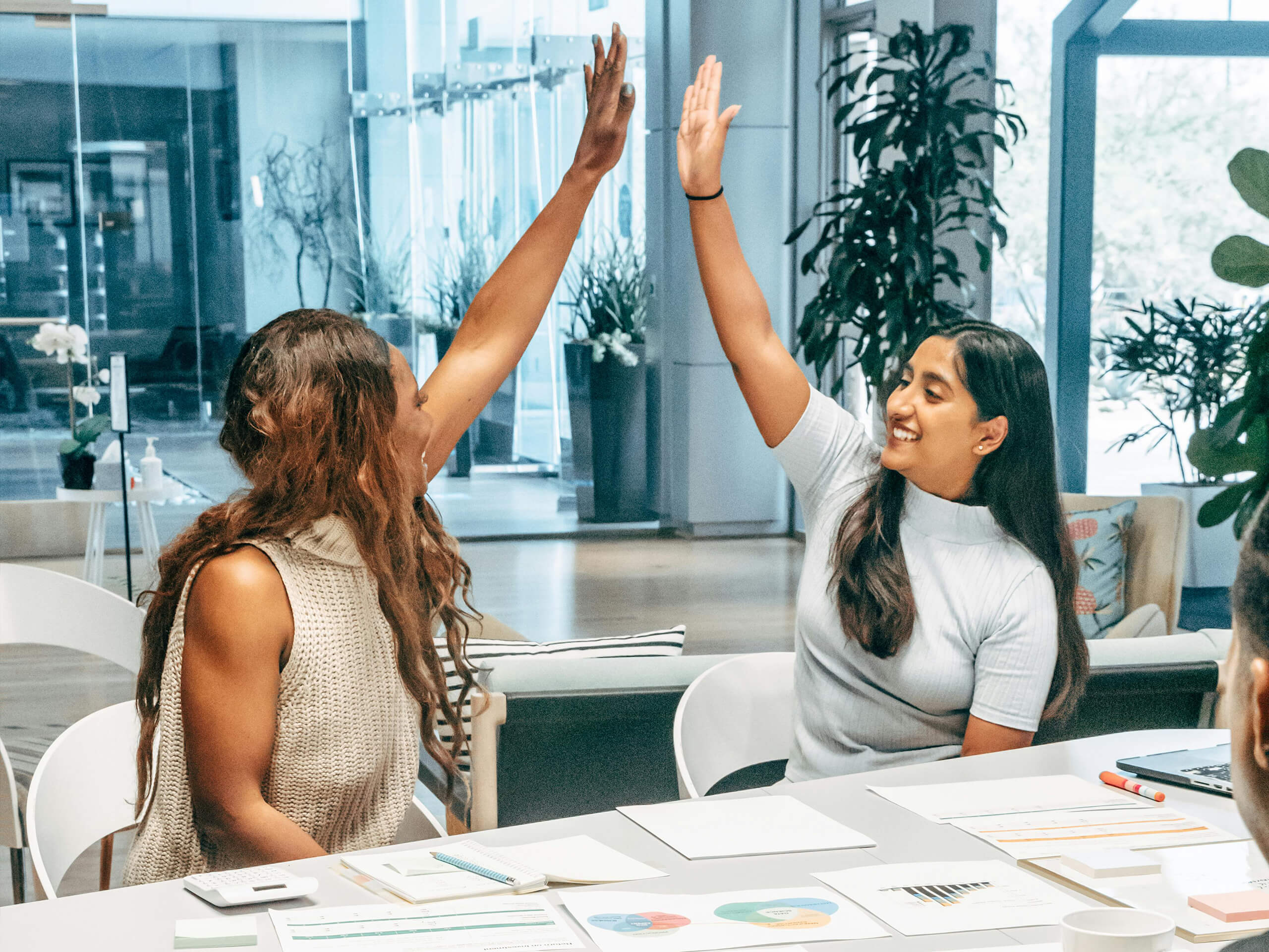 Zwei Frauen geben sich am Besprechungstisch lächelnd eine High Five.